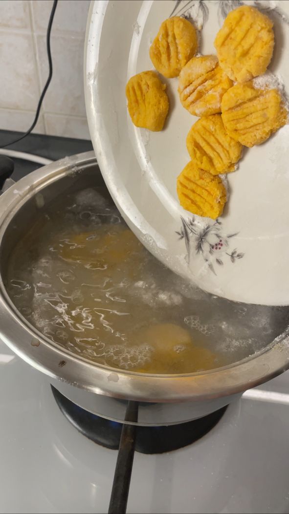Rohe Kürbis-Gnocchi werden vom Teller in kochendes Salzwasser gegeben