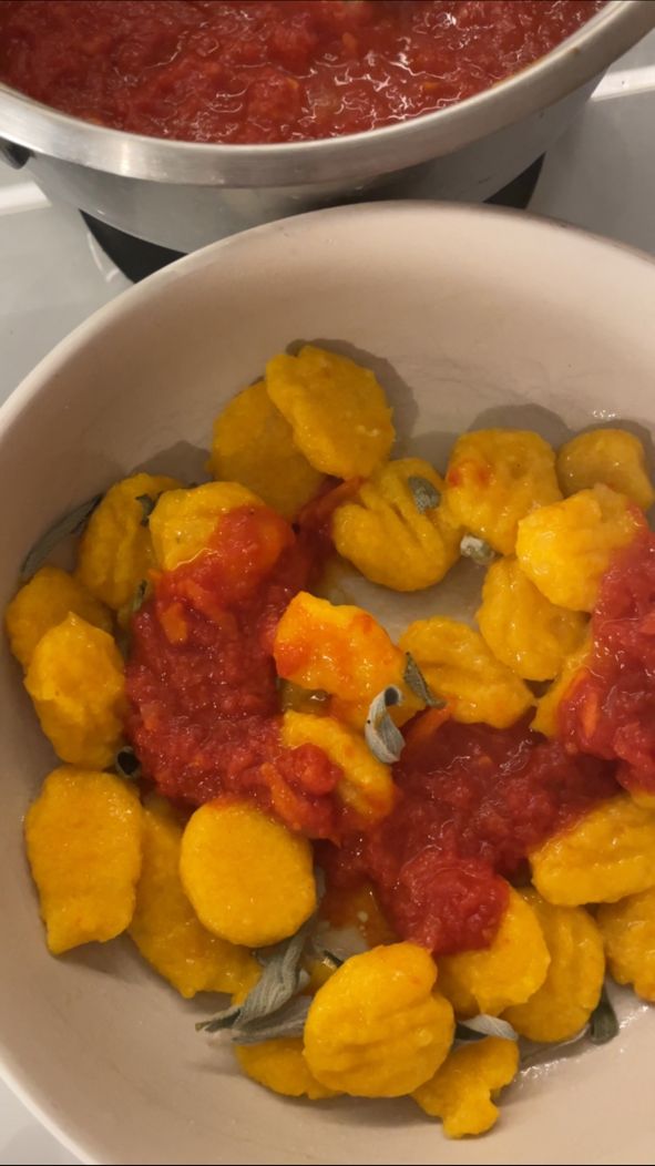 Vegane Kürbis-Gnocchi mit Tomatensauce und Salbei in einer Schale, daneben ein Topf mit Sugo